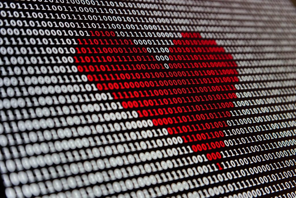 coração em vermelho em fundo branco feito com números binários representando como a inteligência artificial ajuda no desfecho clínico
